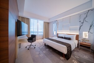 A modern hotel room with a large bed, a desk, a chair, and a TV.