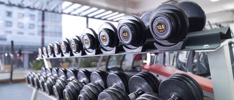 A rack of dumbbells in a gym with a city view through the windows.