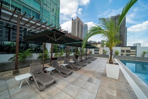 A rooftop pool area with lounge chairs and umbrellas, surrounded by modern buildings.