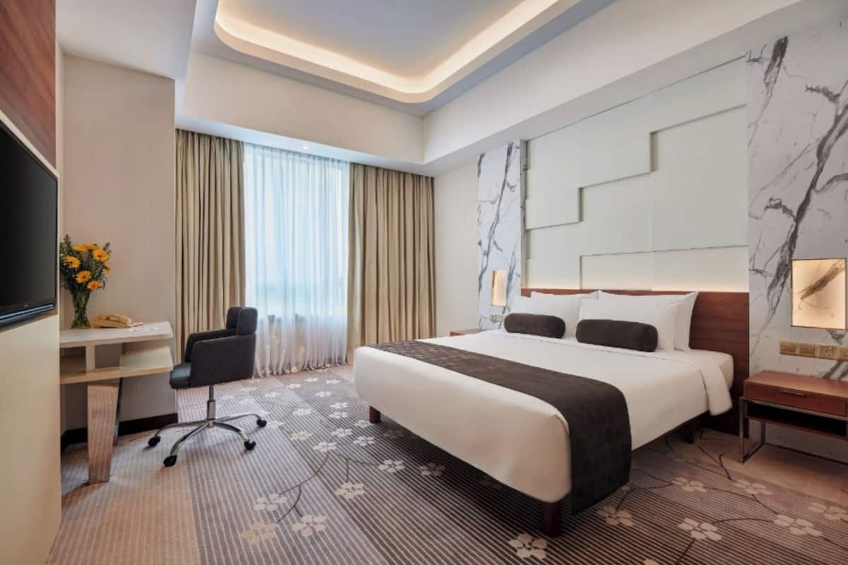 Une chambre d’hôtel avec un grand lit, un bureau, une chaise, une télévision et une fenêtre avec des rideaux.