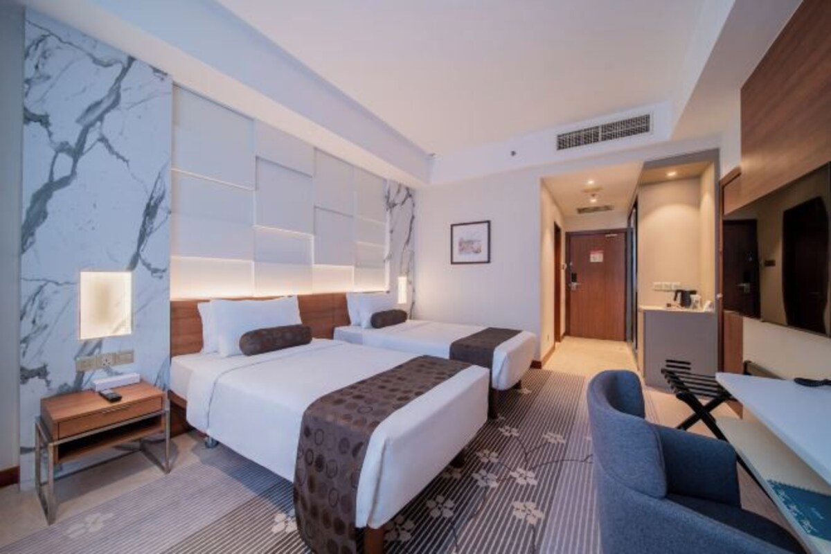Une chambre d’hôtel avec deux lits, un bureau, une chaise, une télévision et une salle de bain visible à travers une porte ouverte.