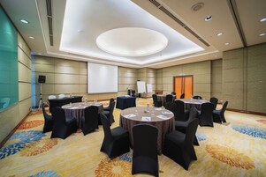 A conference room with round tables, black chairs, and a projector screen.