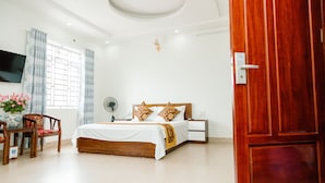 Een slaapkamer met een houten bed, een nachtkastje, een televisie, een ventilator en een raam met gordijnen.