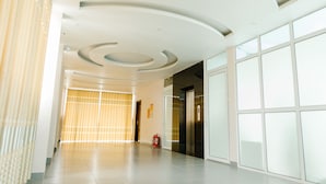 Een ruime, moderne hal met een golvend plafond, een brandblusser en een glazen deur naar een lift.