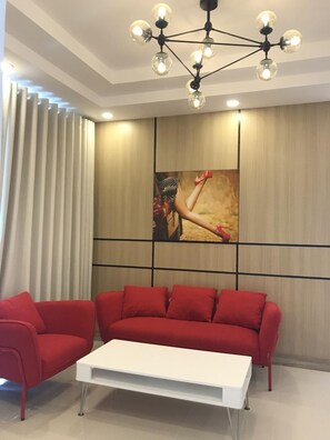 A modern living room with a red sofa set, a white coffee table, and a unique chandelier. - Family Homestay Melody Vung Tau (Ho Chi Minh City)