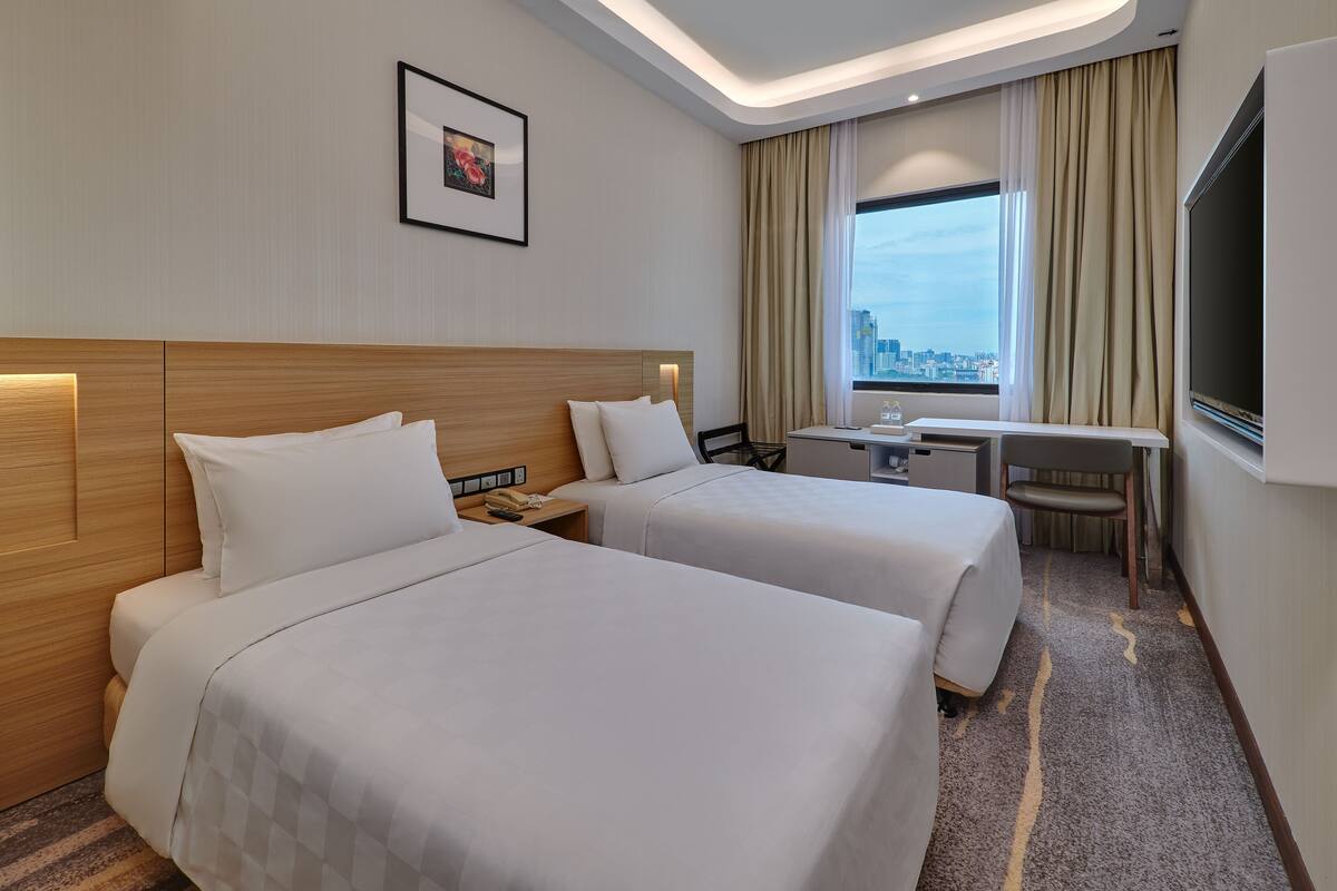A hotel room with two beds, a desk, a chair, a TV, and a city view.