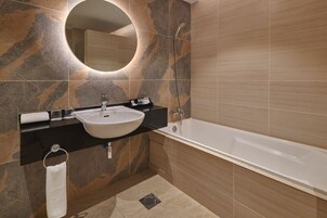 A modern bathroom with a freestanding bathtub, a round mirror, and a black countertop with a sink.