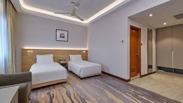 A hotel room with two beds, a desk, a ceiling fan, and a carpeted floor.
