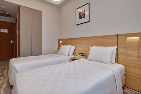 Una habitación de hotel con dos camas, cabecera de madera, mesita de noche con un teléfono y un cuadro enmarcado en la pared.