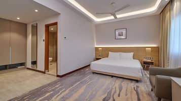 A hotel room with a bed, a desk, a chair, a ceiling fan, a nightstand, and a bathroom visible through an open door.