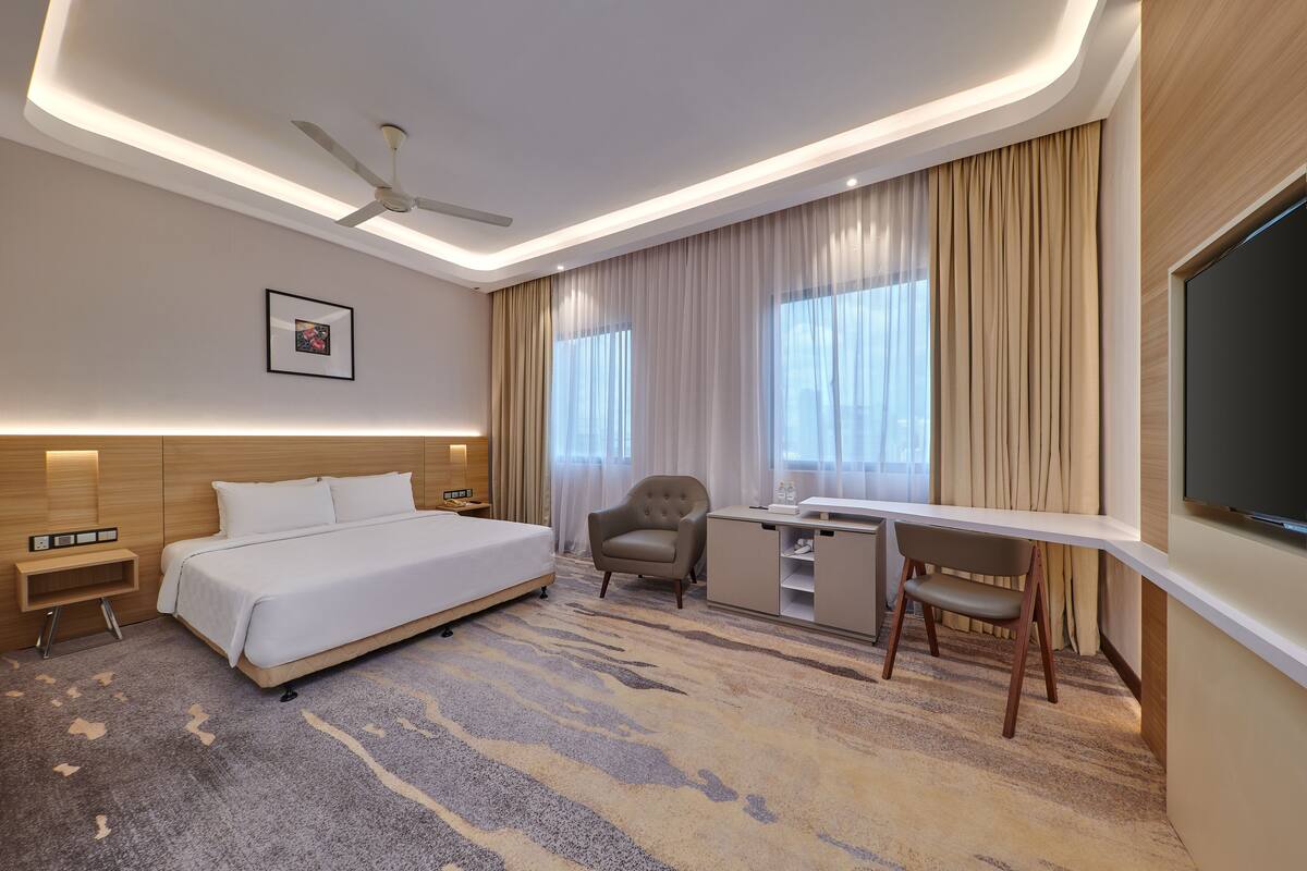 A hotel room with a bed, desk, chair, and a flat-screen TV.