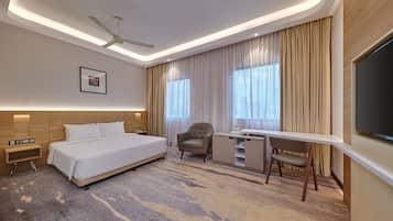 A hotel room with a bed, desk, chair, and a flat-screen TV.