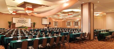 A conference room with multiple tables and chairs, a podium, and a screen displaying a presentation.
