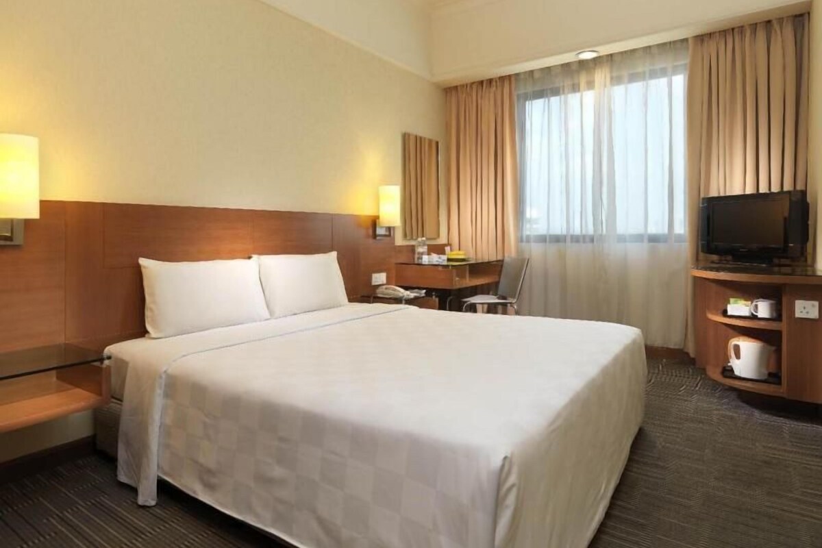 Habitación de hotel con una cama grande, un escritorio con silla, televisión y cafetera.