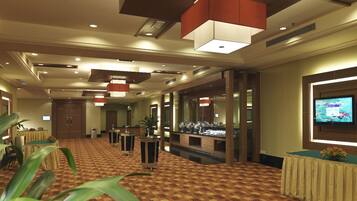 A hotel lobby with a checkered carpet, multiple tables, and a television screen on the wall.
