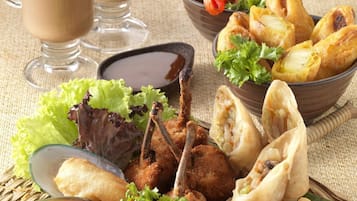 Diversos pratos fritos, incluindo samosas, frango frito e uma salada, acompanhados por dois copos de uma bebida castanha.