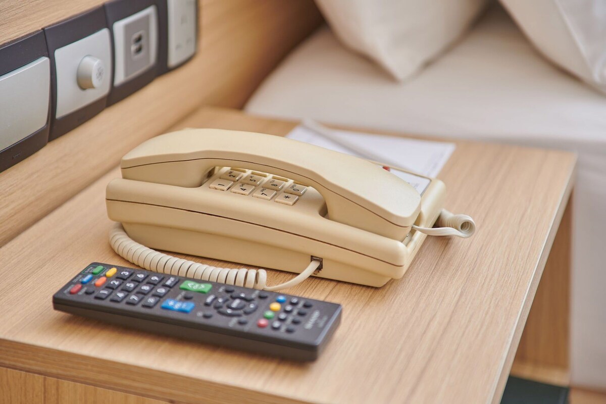 Un téléphone de couleur beige et une télécommande sur une table de chevet en bois, dans une chambre d’hôtel.