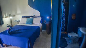 A room with a bed, a nightstand, a lamp, a swan decoration, and a bathroom with a toilet and sink.