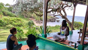 Estudio de yoga con vista al océano, que cuenta con una terraza de madera y un espacio cubierto con colchonetas y esterillas.