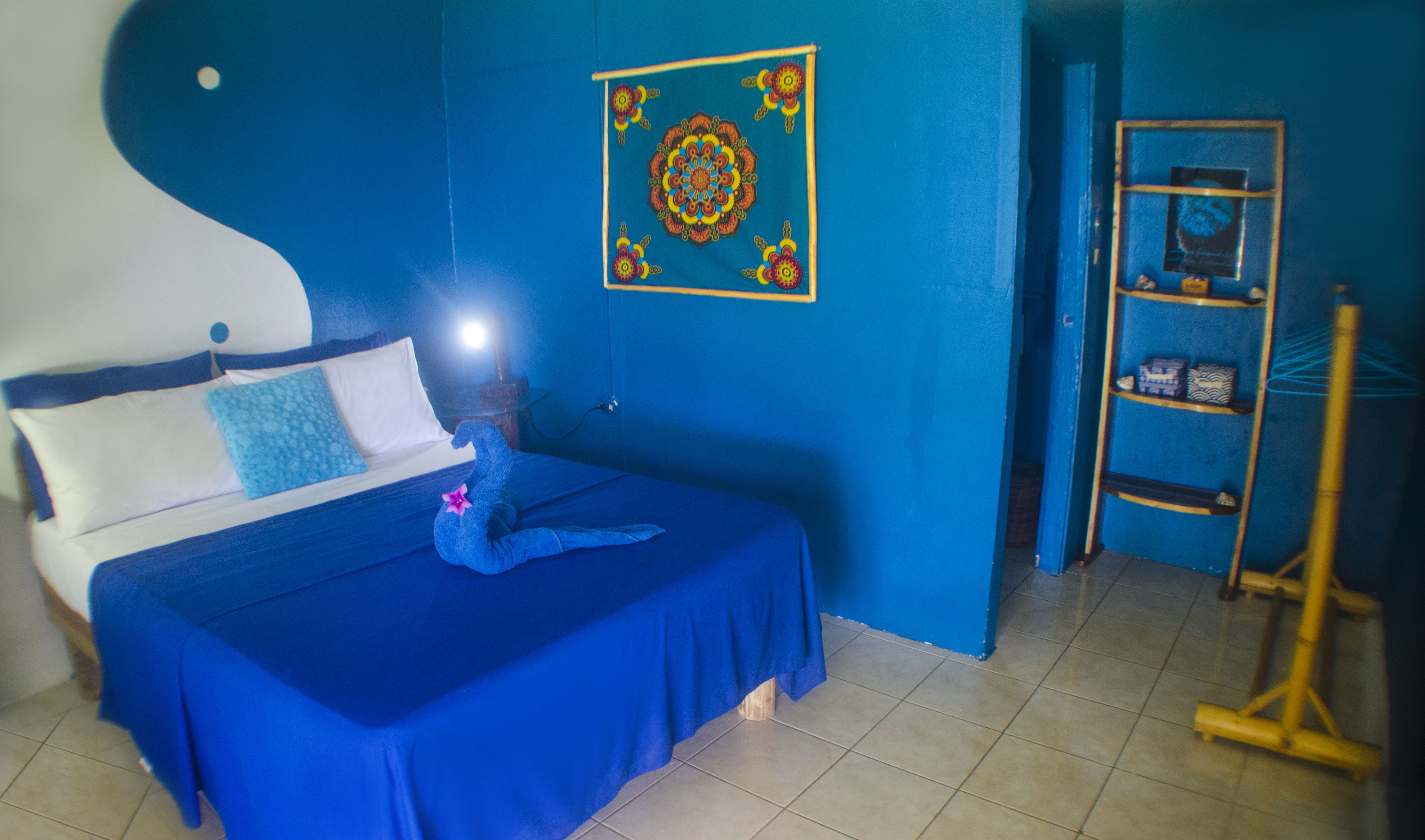 A room with a bed, a blue wall, a wooden ladder, and a shelf with decorative items.
