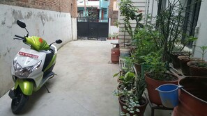 Una patineta estacionada en un callejón estrecho, con macetas a un lado y una entrada cerrada al otro.