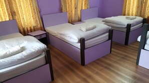 Una habitación con dos camas, cada una con ropa de cama blanca y cabecero. Entre las camas, hay una mesita de noche con cajón. Las paredes son moradas y el suelo es de madera.