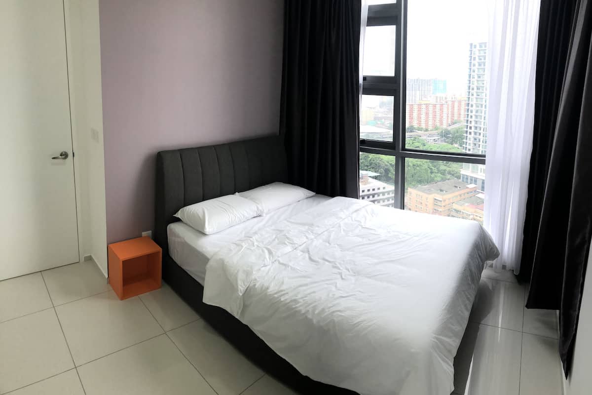 A bedroom with a bed, a nightstand, a window with curtains, and a view of buildings outside.
