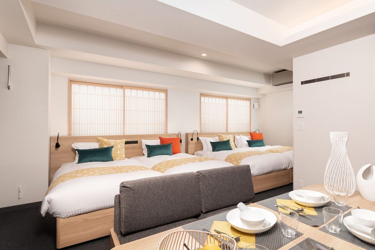 A modern hotel room with two beds, a dining area, and a view of the city.