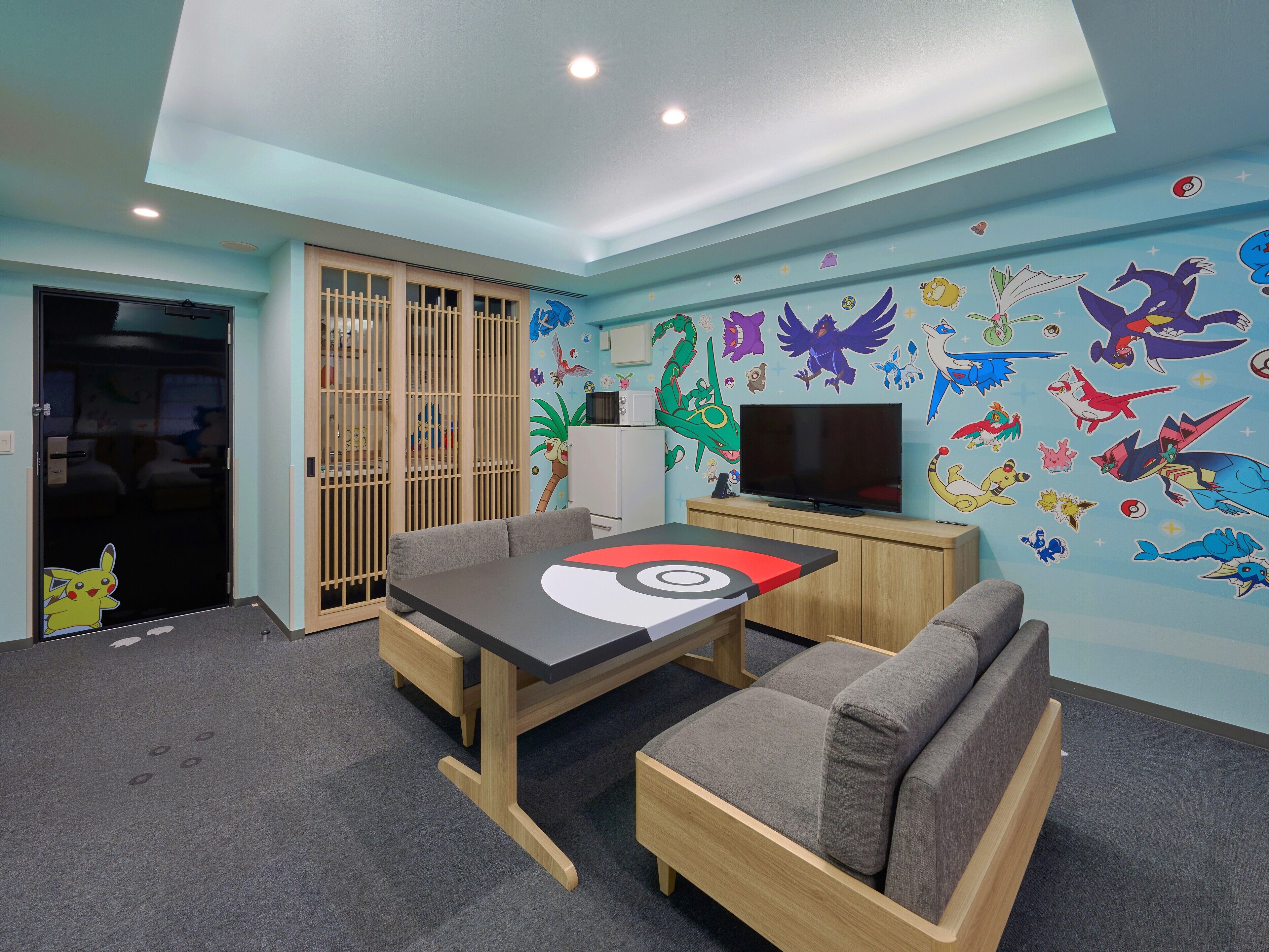 Een kamer met een televisie, een tafel, twee stoelen en een muur versierd met Pokemon stickers.