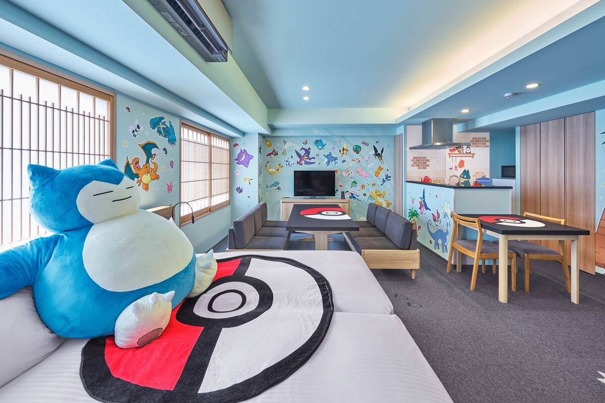 Una habitación con sofá, un juguete de peluche grande, televisor, zona de comedor y cocina.