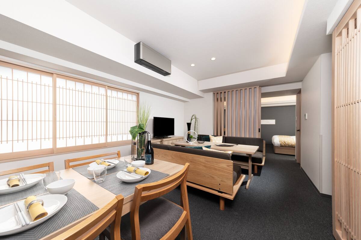 Un comedor moderno con una mesa de madera preparada para cuatro personas, un sofá y un televisor.