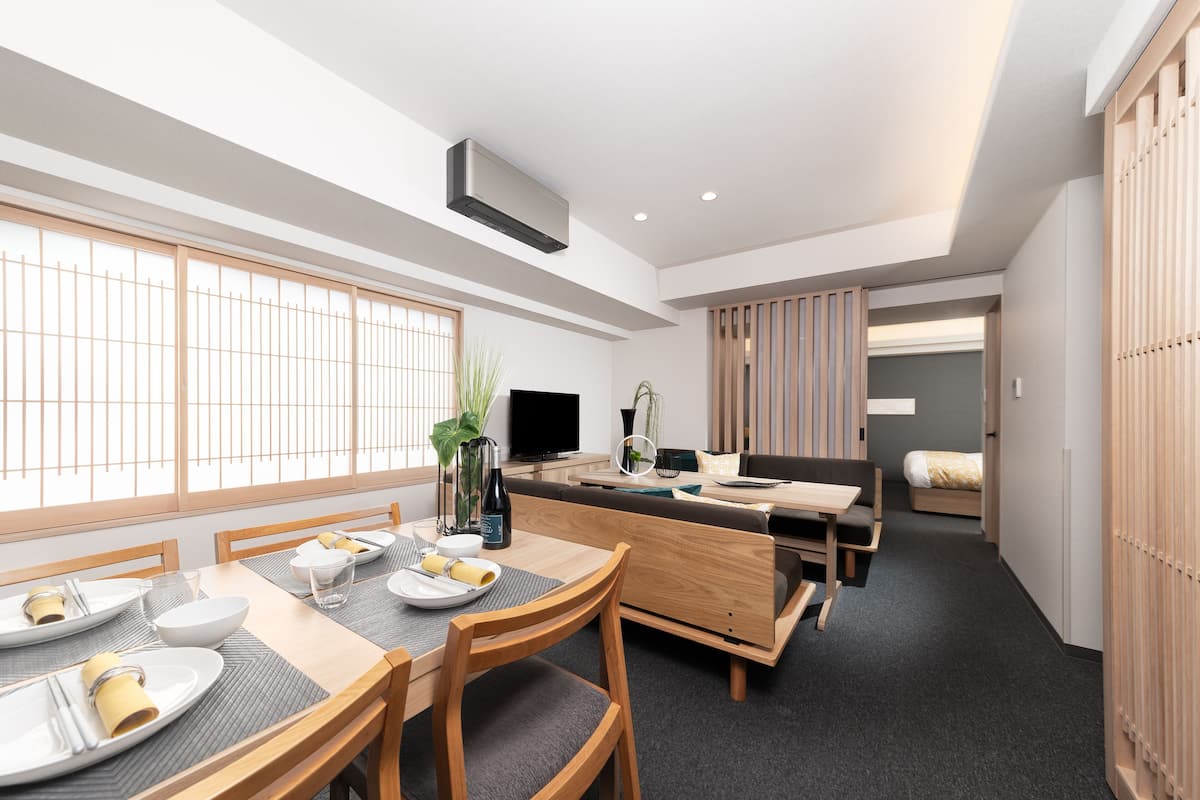 A modern dining area with a wooden table set for four, a sofa, and a TV.
