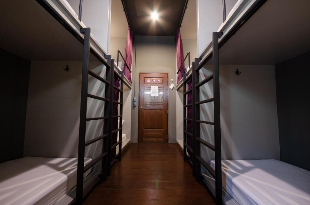 A narrow hallway with bunk beds on either side, a wooden door at the end, and a ceiling light.