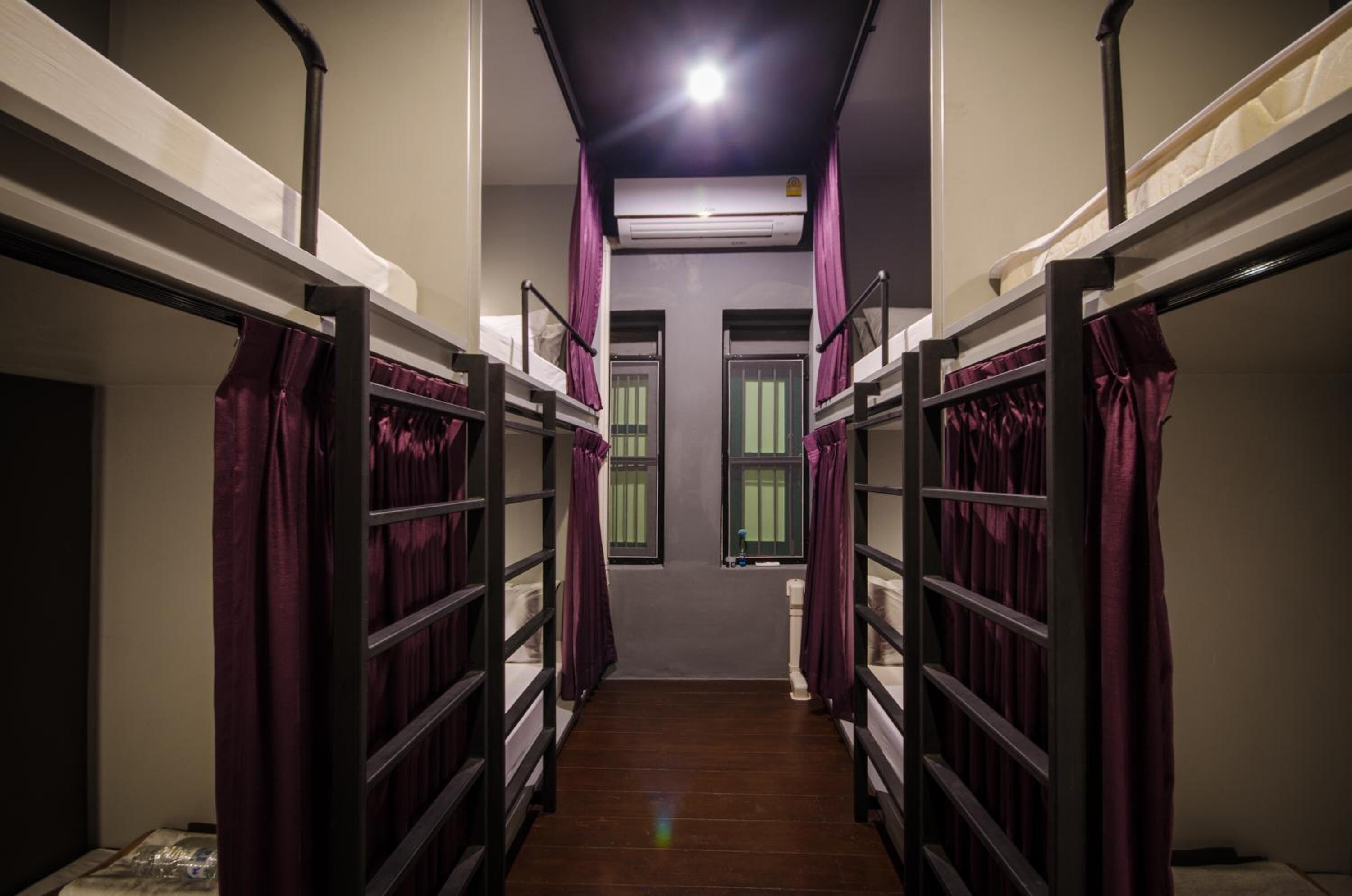 A narrow corridor with bunk beds on either side, each with purple curtains.