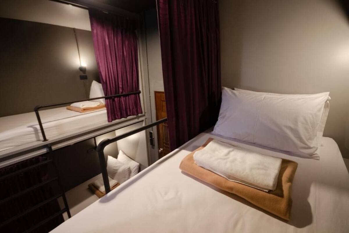 A bunk bed with a mattress and pillows, a wooden headboard, and a window with curtains.