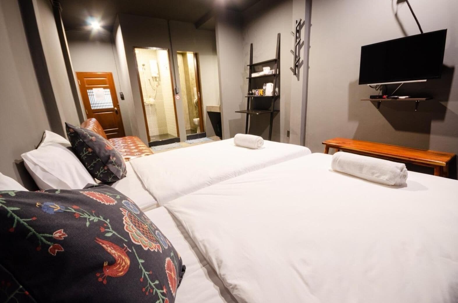 Quarto de hotel com duas camas, uma televisão fixada na parede e um banco de madeira.