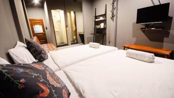 Quarto de hotel com duas camas, uma televisão fixada na parede e um banco de madeira.