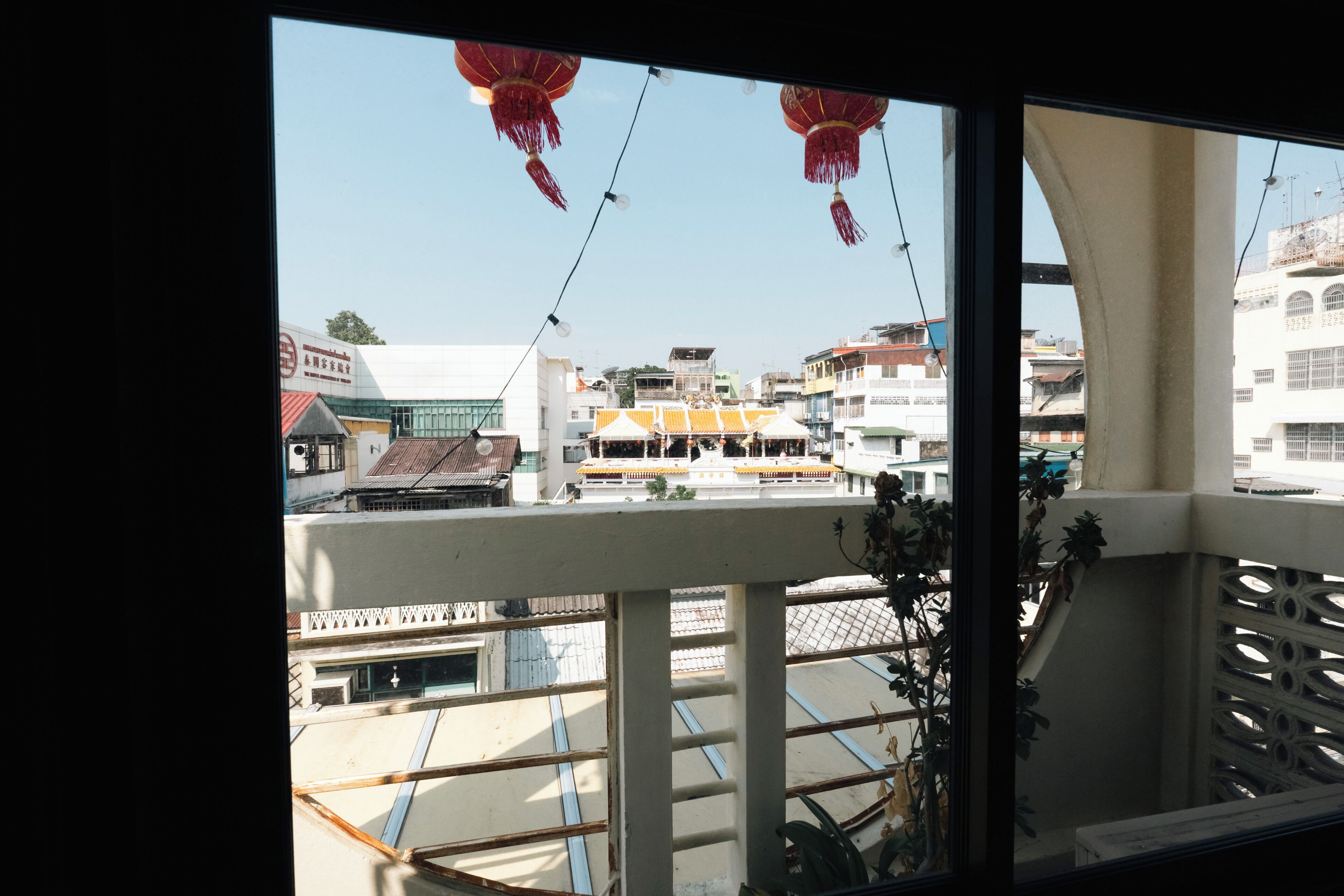 Vista dalla finestra con balcone, che mostra una scena di strada con edifici, un tendone giallo e lanterne rosse.