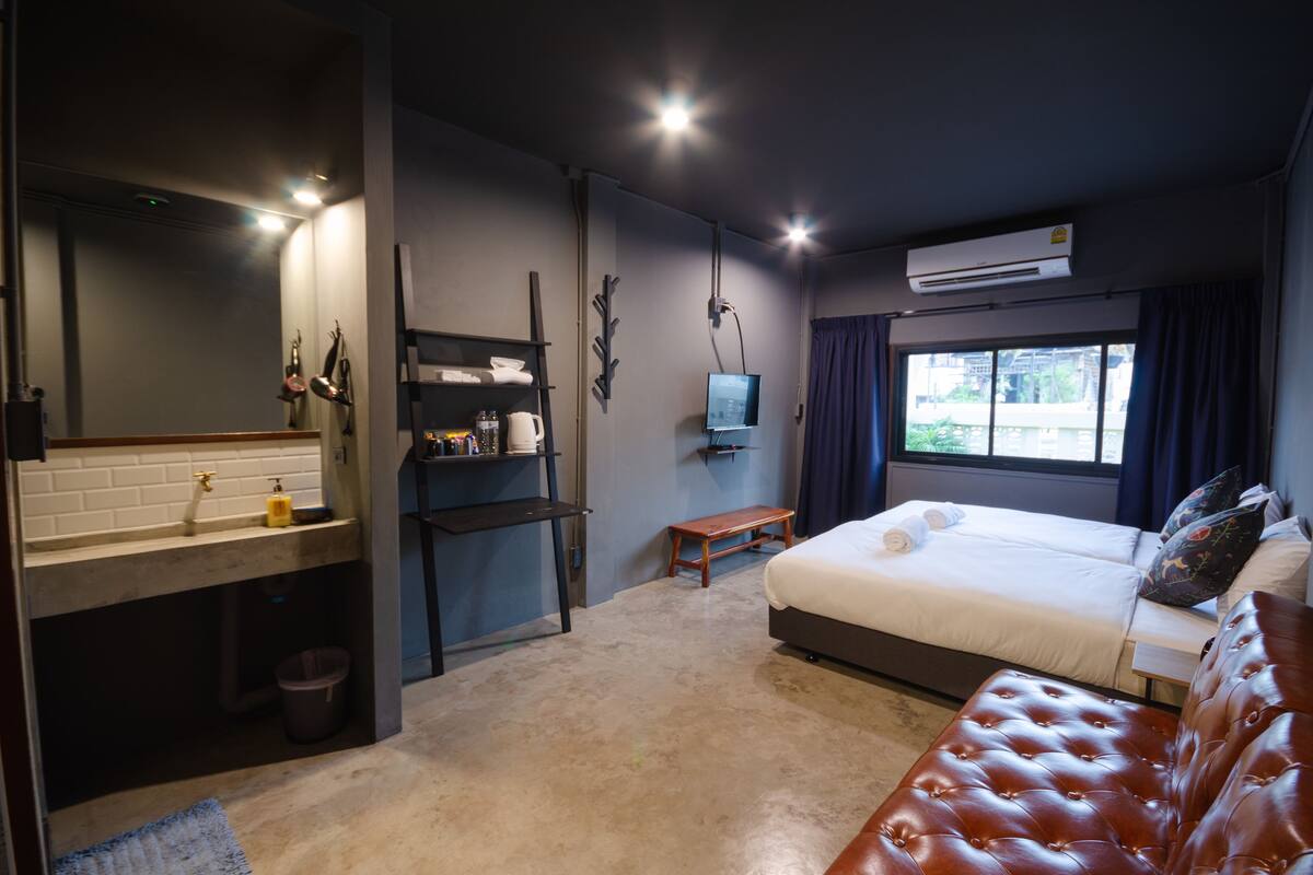 A modern hotel room with a large bed, a small desk, a vanity with a mirror, and a window with curtains.