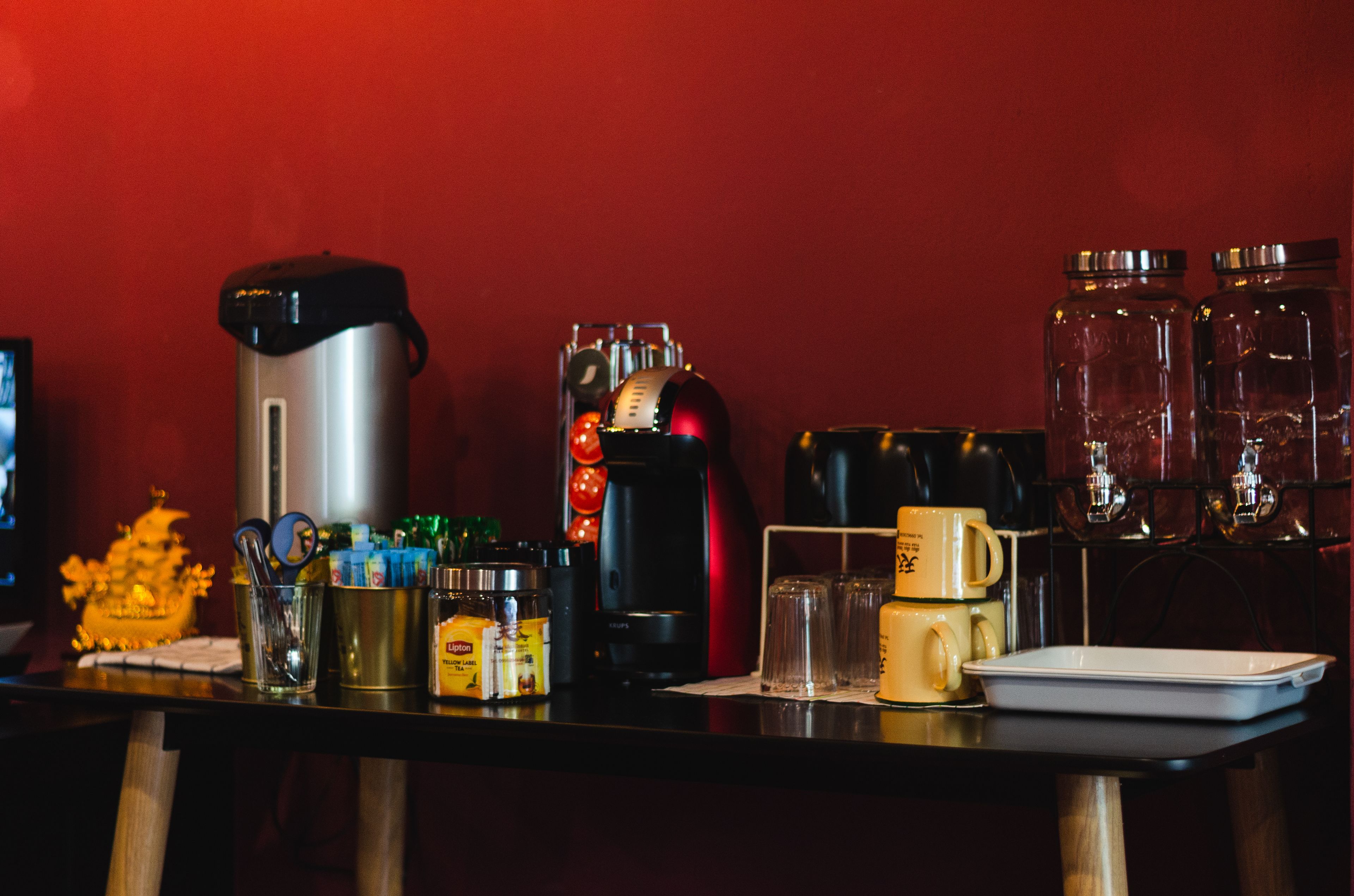 En köksbänk med olika apparater och behållare, inklusive en kaffebryggare, en vattenkokare och burkar.