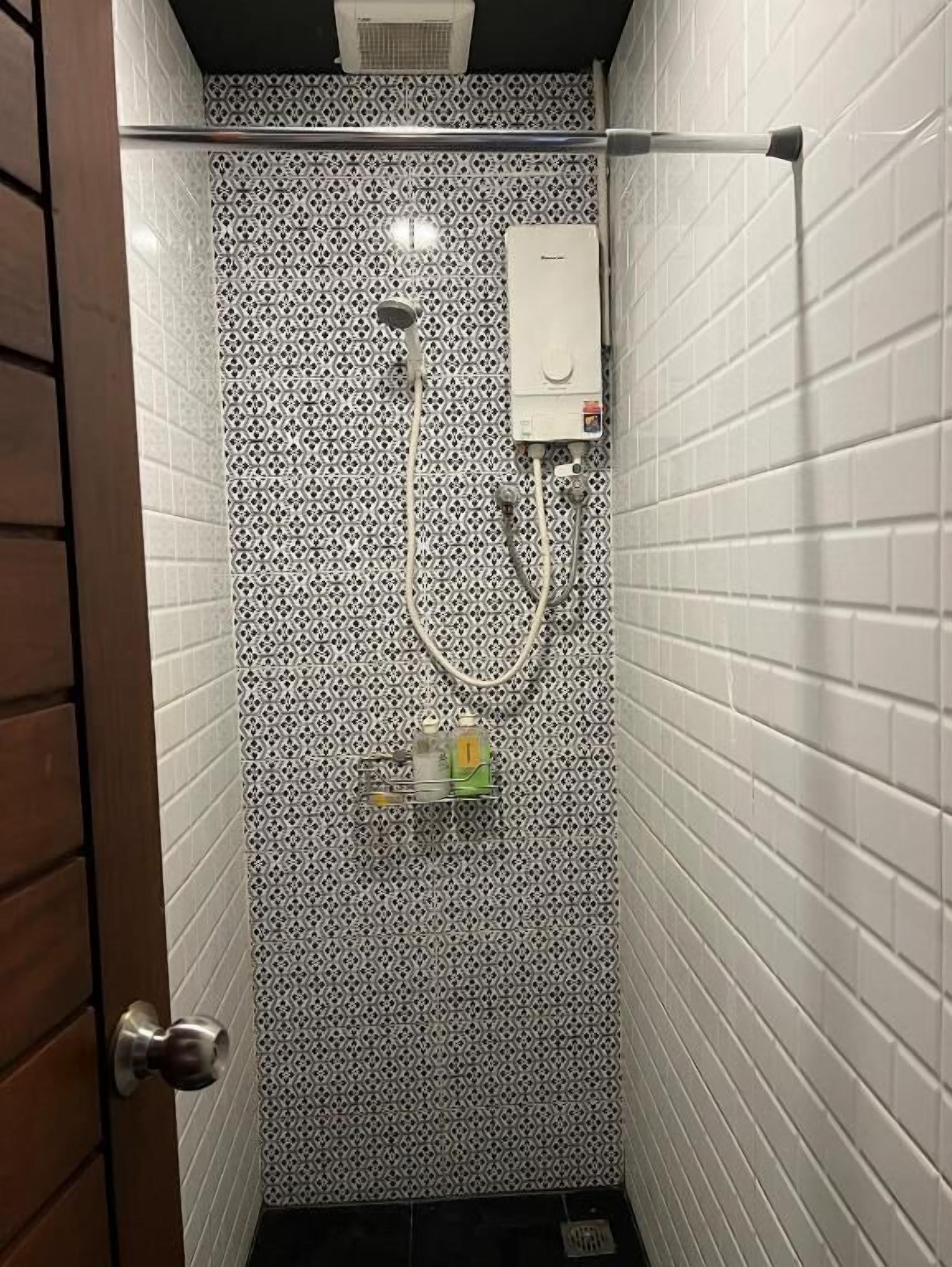 A shower with a patterned wall, a handheld showerhead, and a control panel.