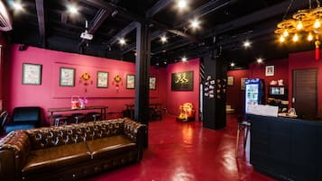 A room with a red wall, a brown leather couch, a bar area, and a ceiling with exposed beams and lighting fixtures.