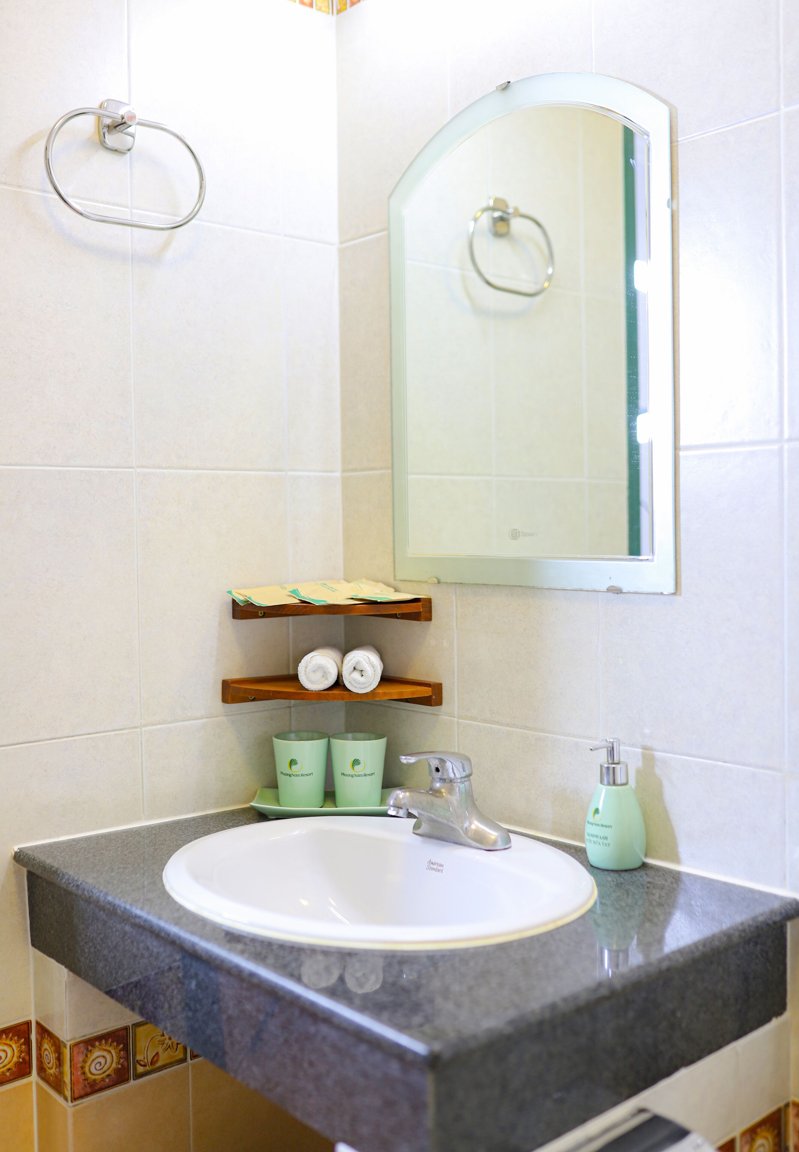 Een badkamer met een wastafel, spiegel, handdoekrek en planken met toiletartikelen.