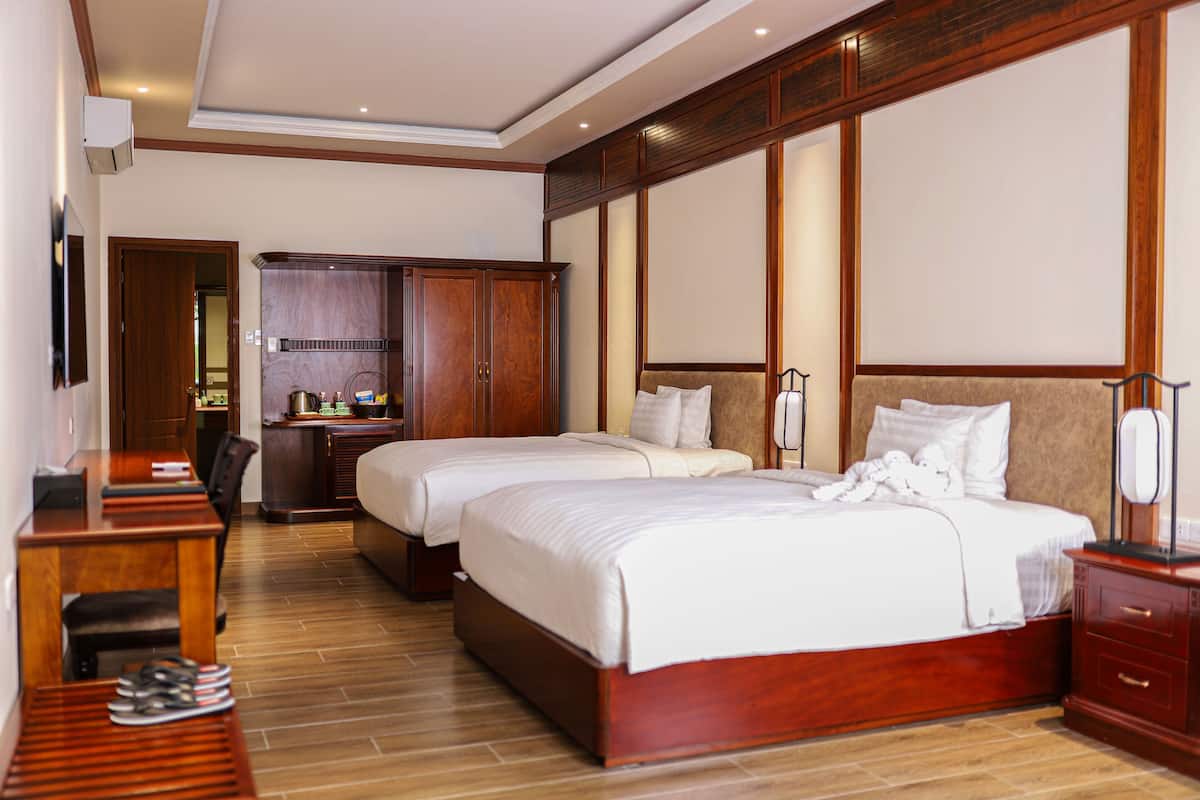 A hotel room with two beds, a desk, a wardrobe, and a small kitchenette.