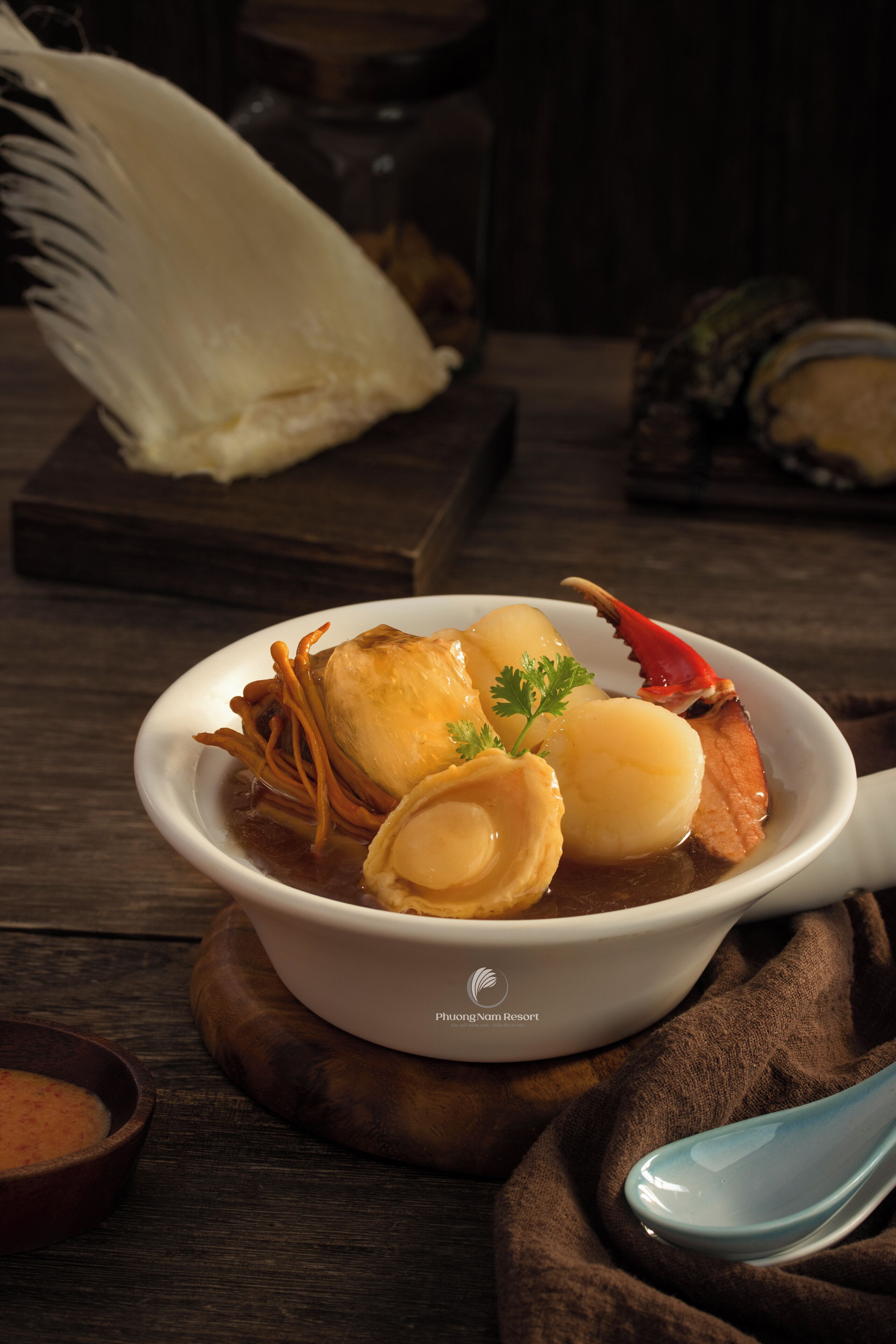 A bowl of seafood soup with a crab leg, dumplings, and a garnish on a wooden table.