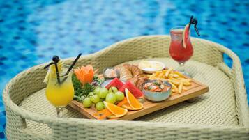 Una bandeja de mimbre con diversos alimentos y bebidas, junto a una piscina.