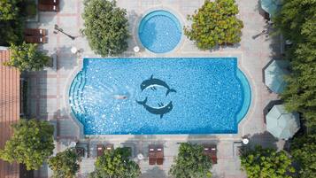 Piscina retangular com golfinhos, rodeada por árvores e coberta por um telhado.
