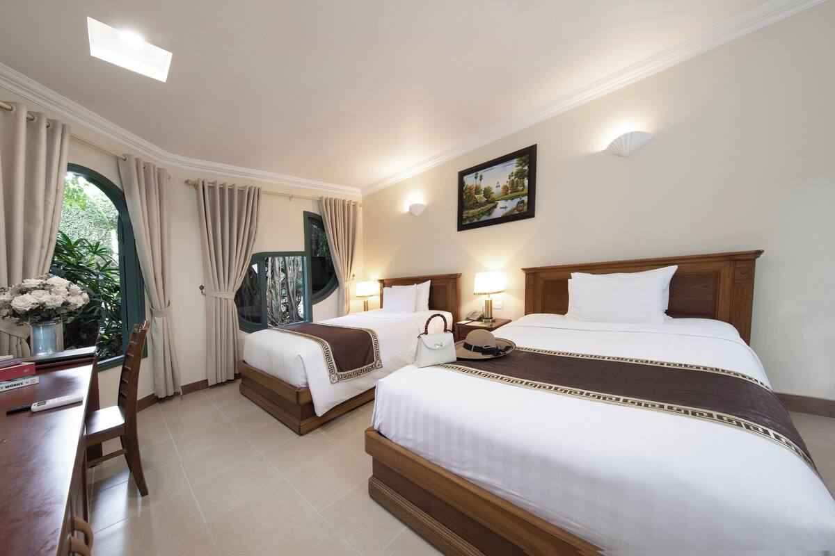 A hotel room with two beds, a desk, and a window with curtains.