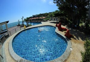 A circular swimming pool with a tiled edge, surrounded by a paved deck and red chairs. - Tanjung Kodok Beach Resort (Paciran)