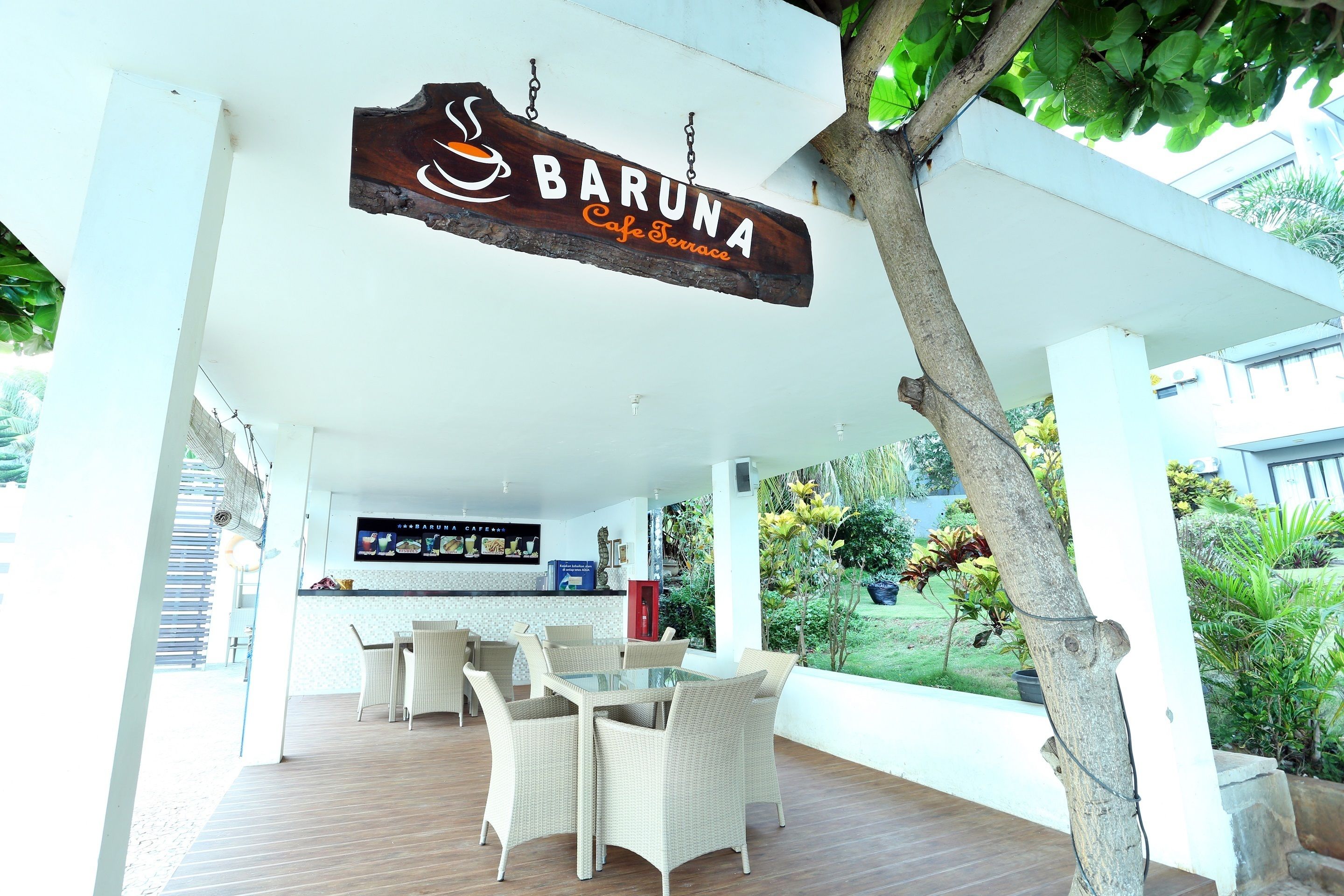 Un área de estar al aire libre techada con mobiliario de mimbre y un letrero de bar que dice "BARUNA Cafe Terrace".